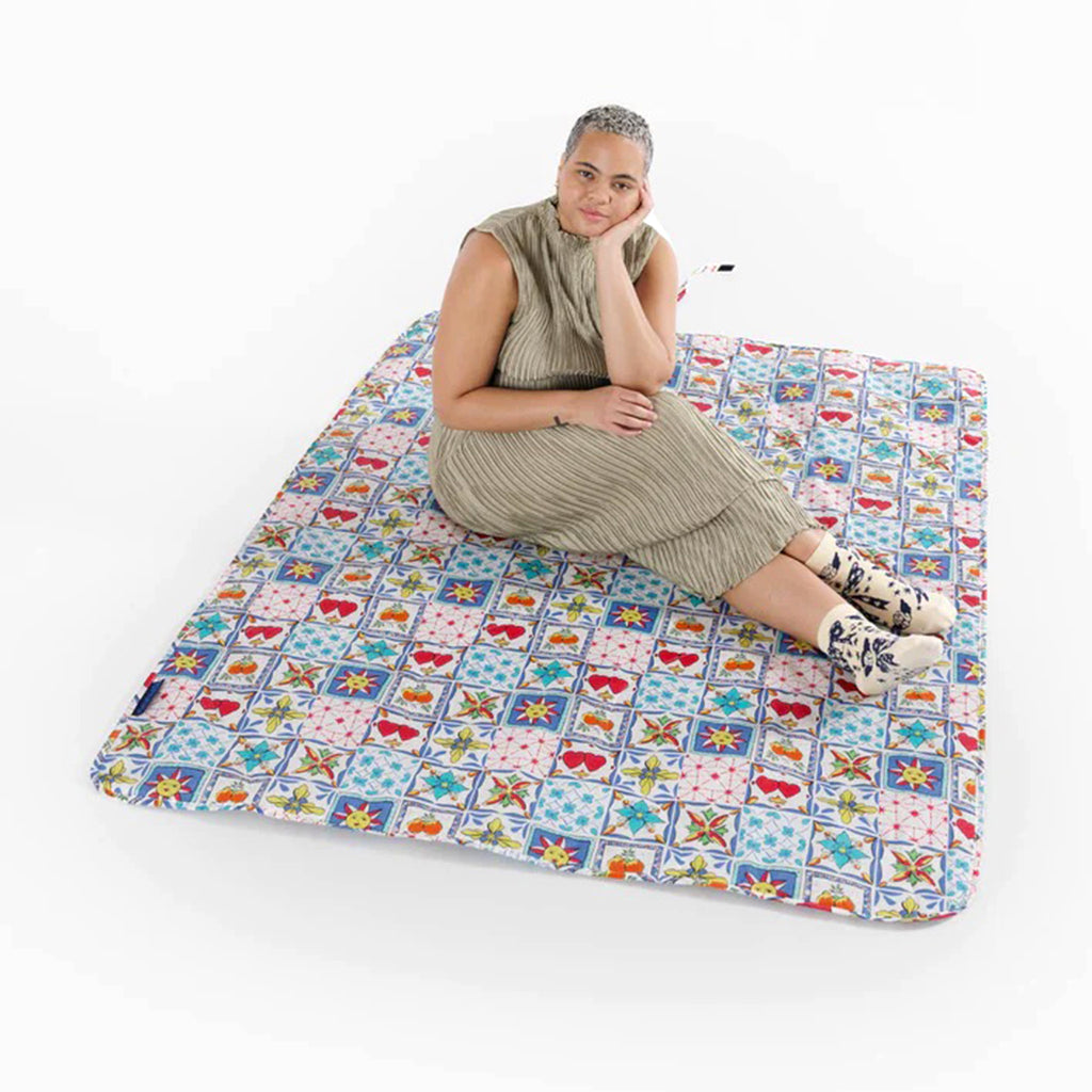 Baggu sunshine tile puffy recycled ripstop nylon and polyester picnic blanket, flat with a model sitting on it.