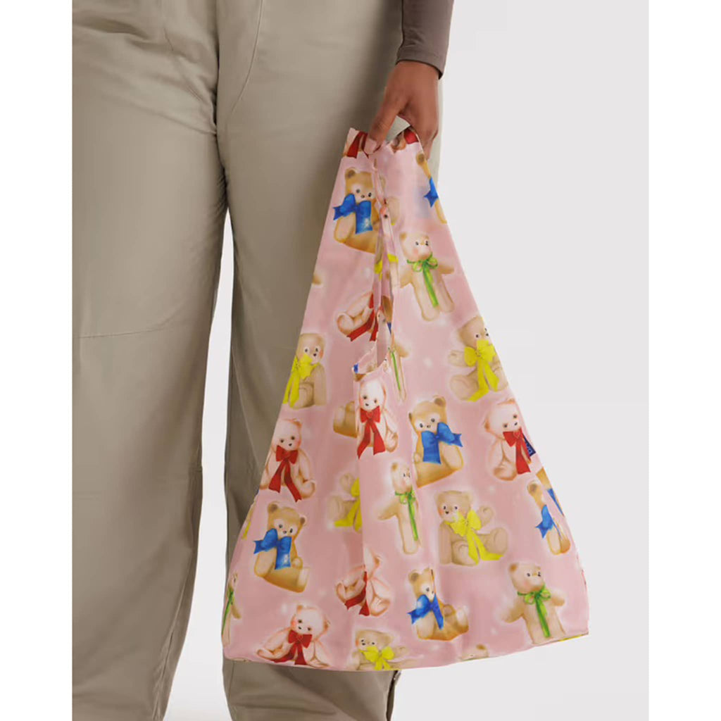 Person holding a pink reusable bag with teddy bear pattern on a white background.