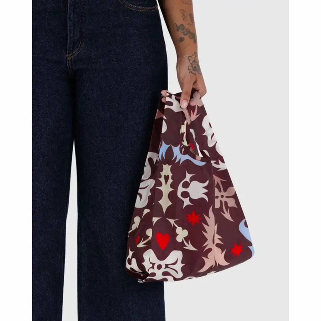 Person holding a patterned bag with dark jeans on a white background.