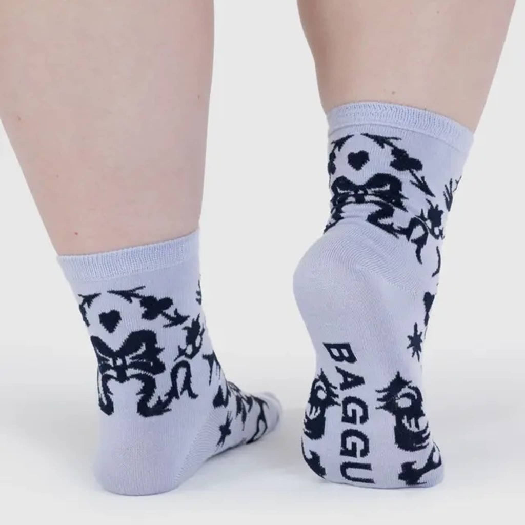 Light purple socks with black floral patterns worn by a person on a white background.