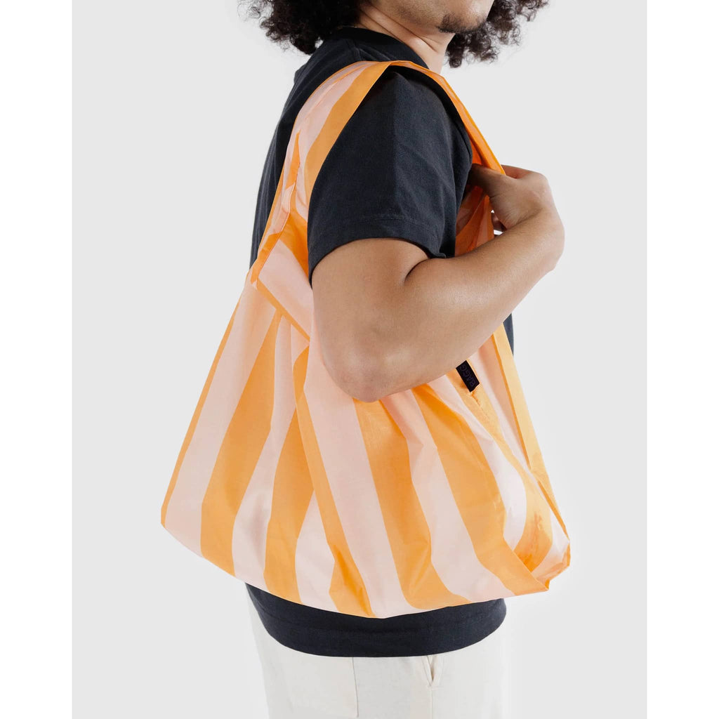 Baggu standard size eco-friendly recycled ripstop nylon reusable tote bag in Tangerine Wide Stripe, on model's shoulder.