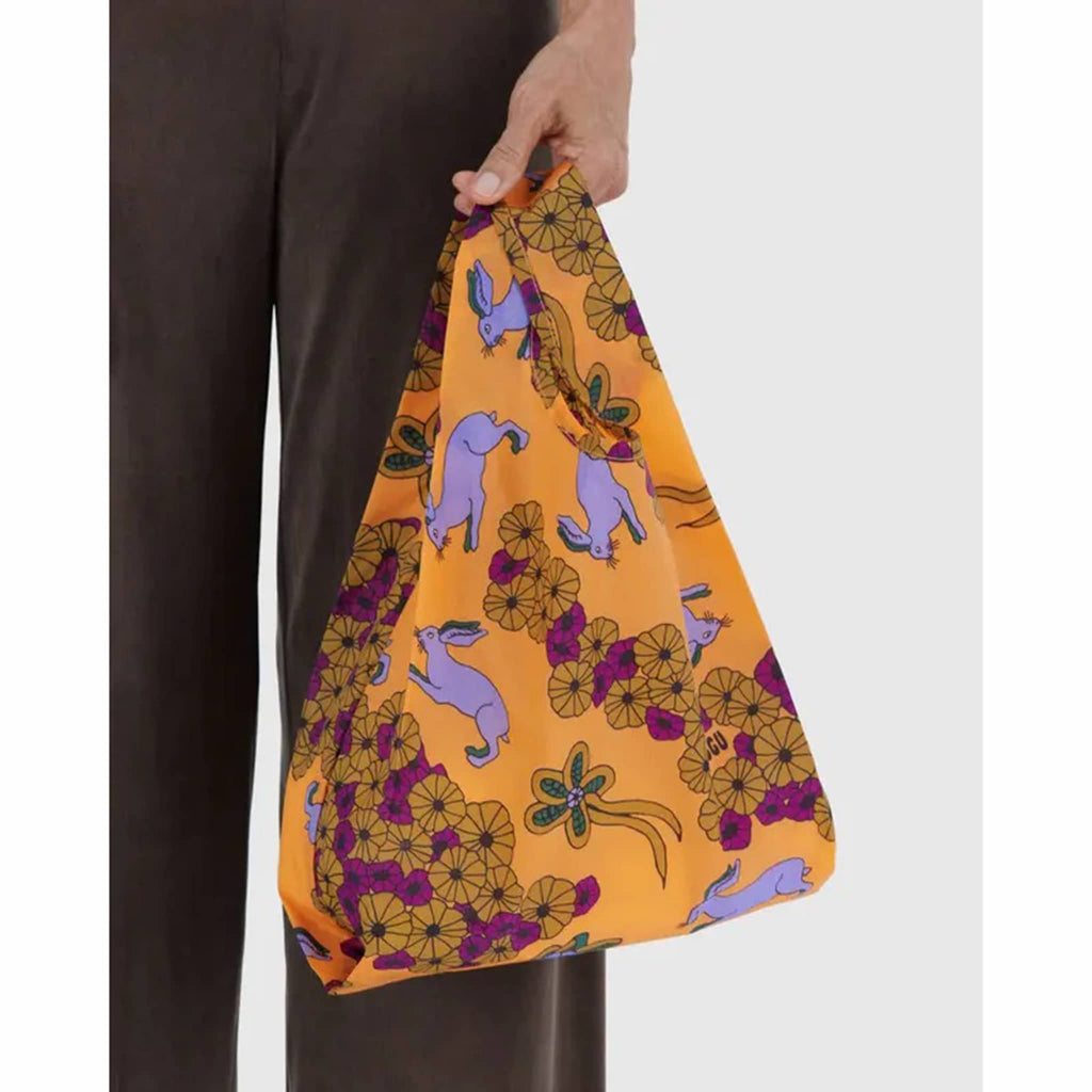 Hand holding a colorful fabric bag with floral and animal patterns on a white background.