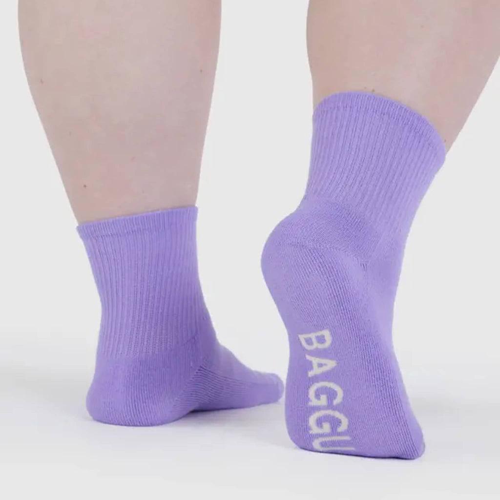 Purple socks with 'BAGGU' branding on a model, on white background.