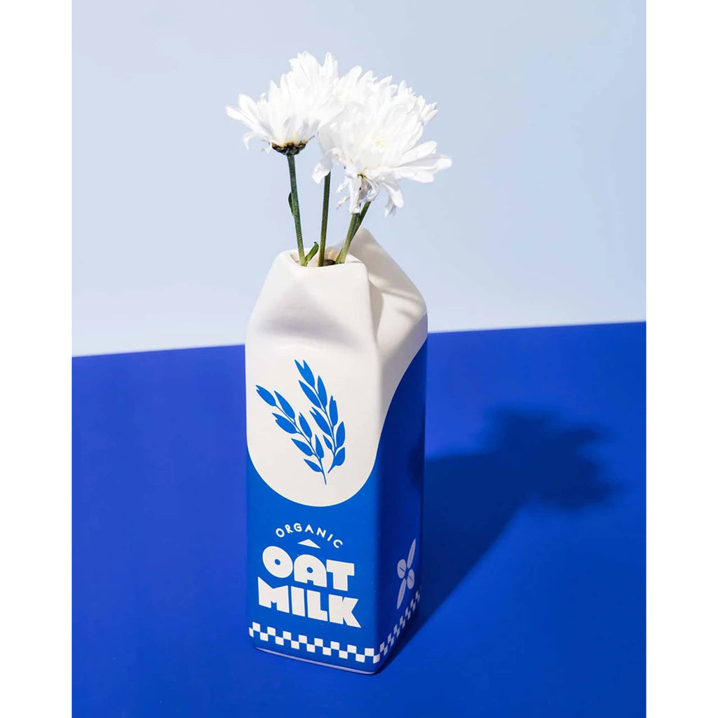 Ban.do blue and white porcelain vase that looks like a carton of oat milk, front angle view with white flowers on a blue background.