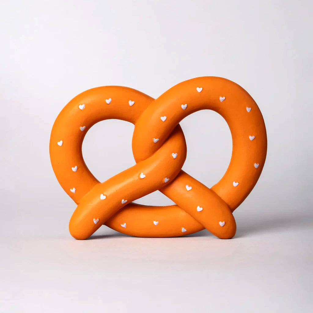 Orange pretzel-shaped soft squishy fidget toy with white heart salt on a light gray background.