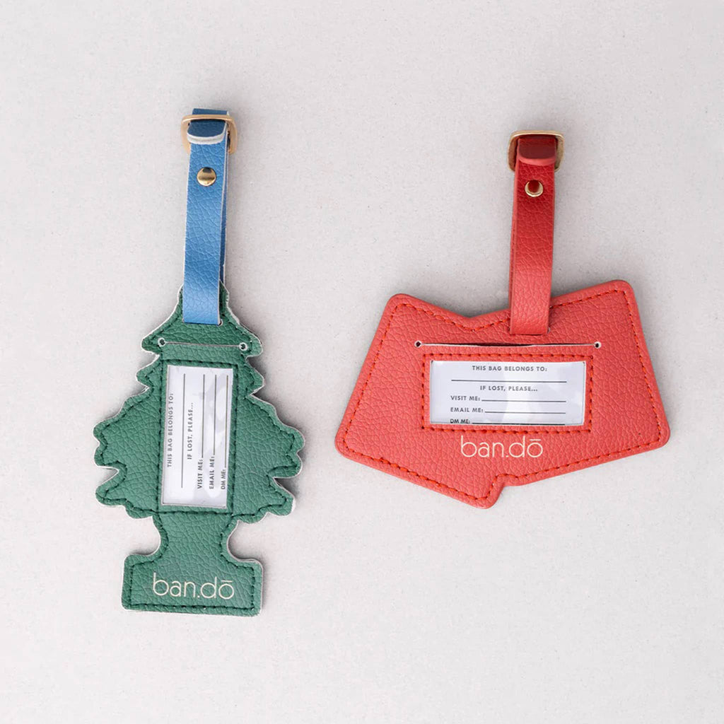 Two luggage tags, one tree-shaped green and one red dice-shaped with info insert, on a gray background.