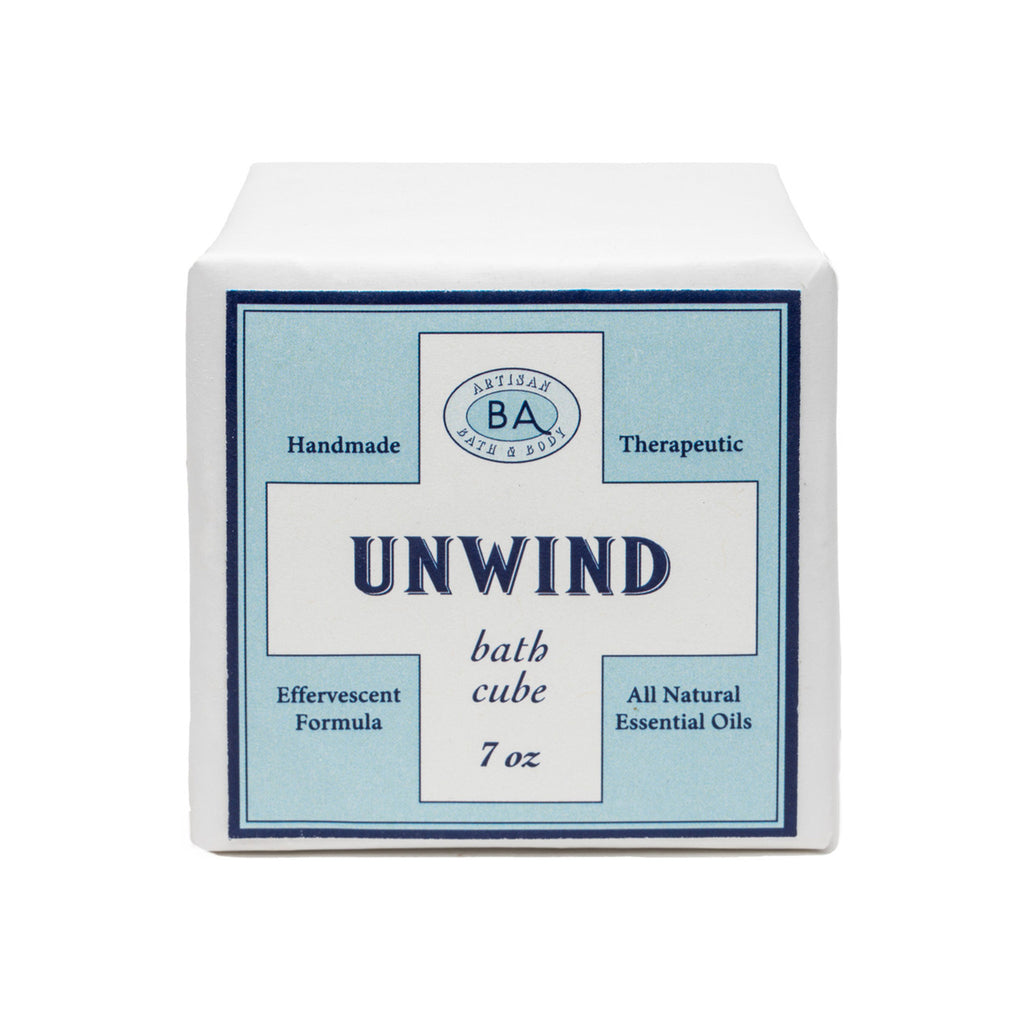 Baudelaire Unwind therapeutic, effervescent bath cube in white paper wrapping with light blue label, front view.