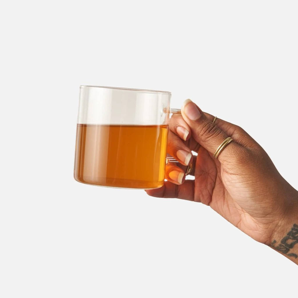 Hand holding a glass mug with brewed tea against a white background.
