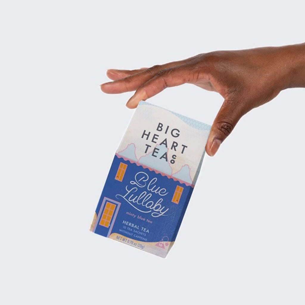 Big Heart Tea Company Blue Lullaby minty blue herbal tea bags packaged in a blue box that looks like a house with snow on it, being held in an outstretched hand.
