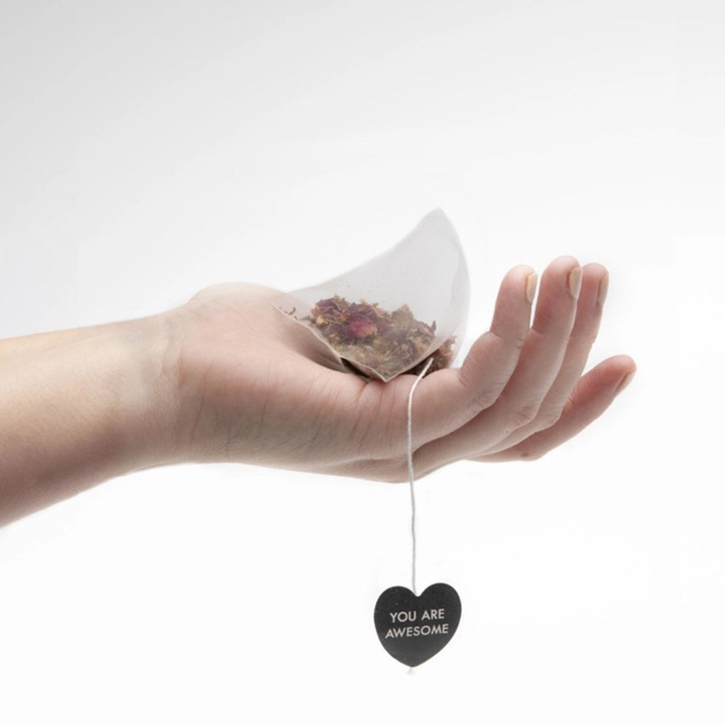 Big Heart Tea Company Blue Lullaby herbal tea bag being held in the palm of a hand with the string hanging down and a paper heart with tea company name at end of string.