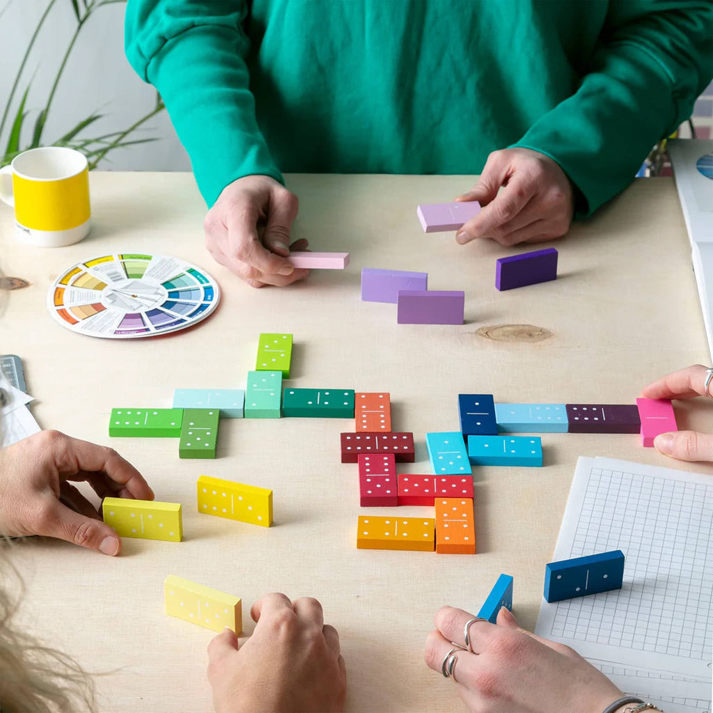 Colorful dominoes being played on a wooden table with participants' hands visible.