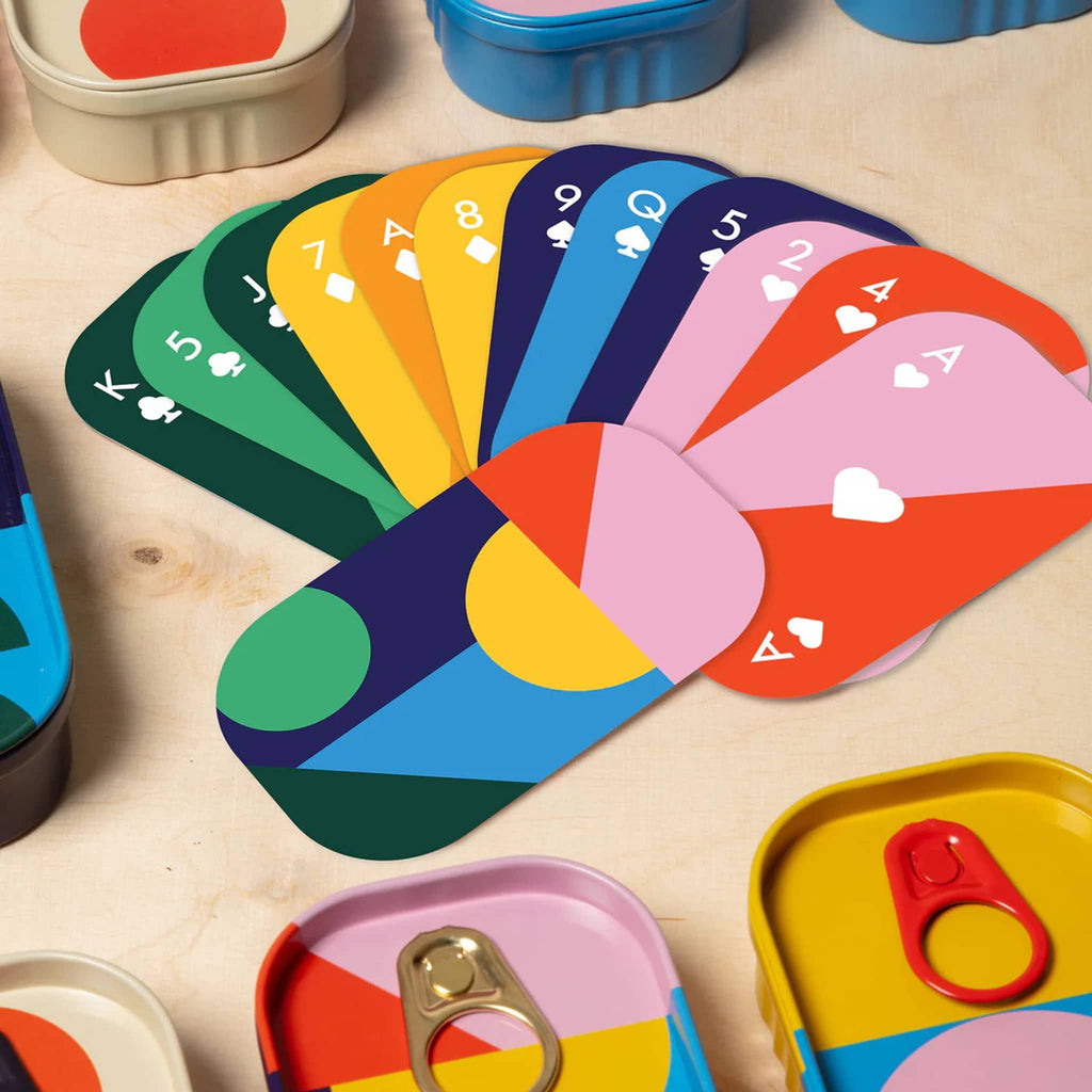 Colorful playing cards fanned out on a wooden surface with colorful containers.