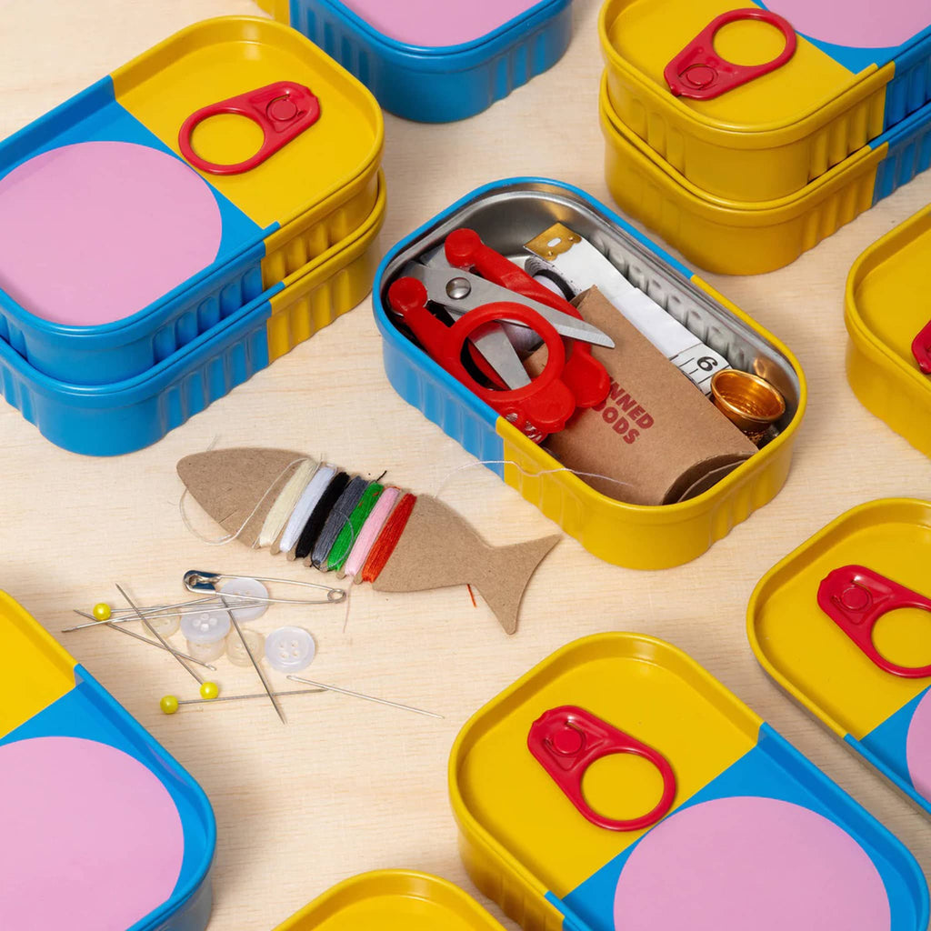Colorful sewing kit with scissors, thread, and pins, with colorful tins around it, on a wooden surface.