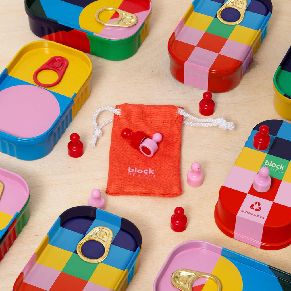 Colorful game pieces with drawstring bag surrounded by colorful tins on a wooden surface.