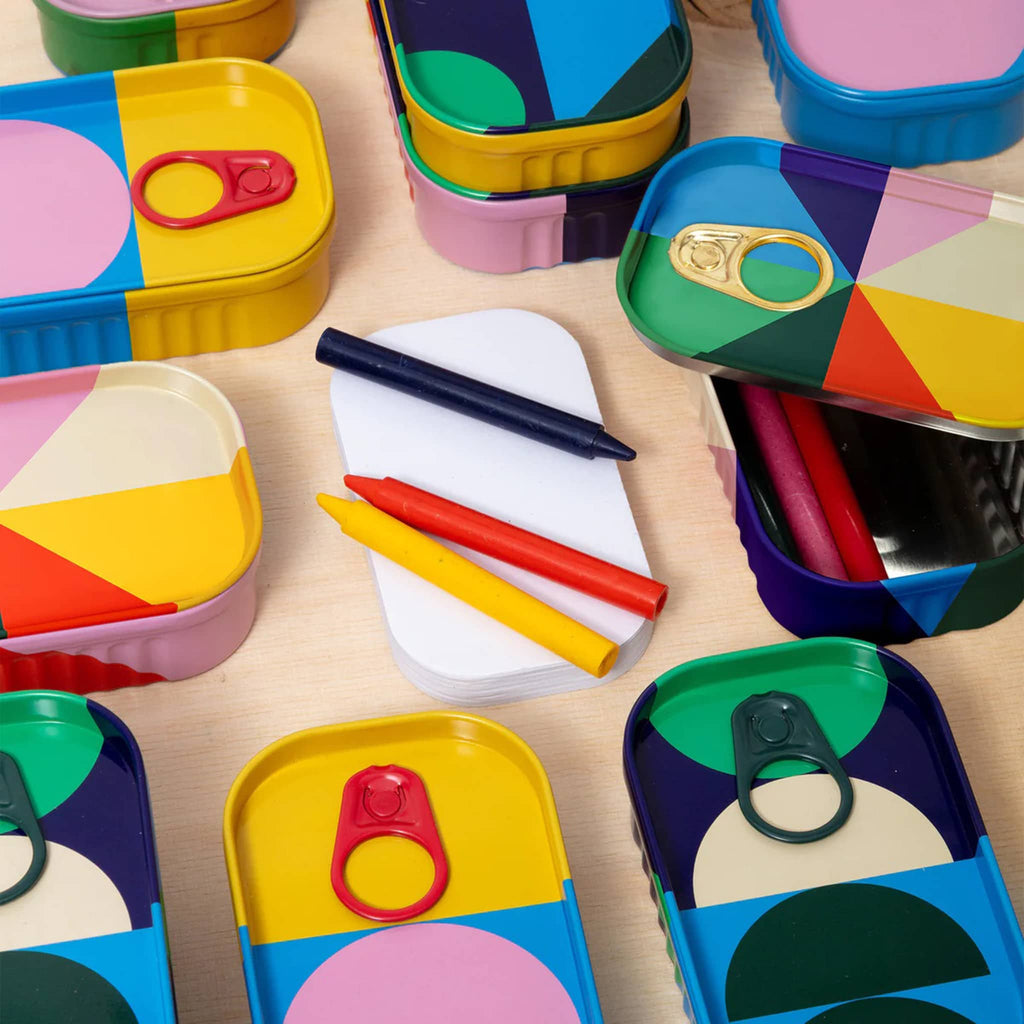 Colorful geometric-patterned containers with crayons and drawing pad on a wooden surface.