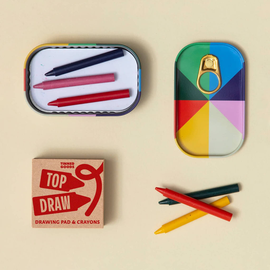 Colorful crayons and white drawing pad with colorful tin packaging on a beige background.