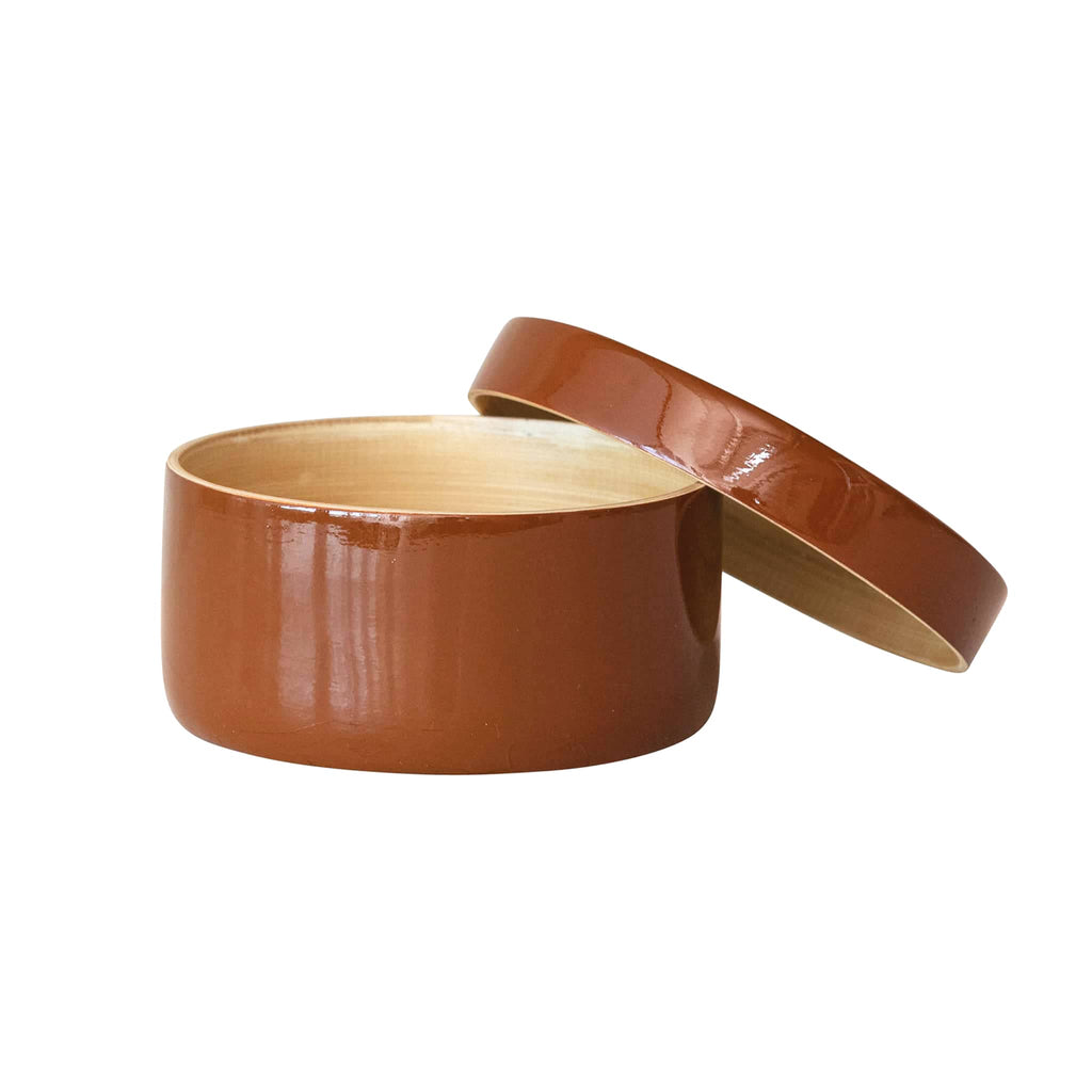 Round caramel brown lacquered container with lid leaning on it, on a white background.