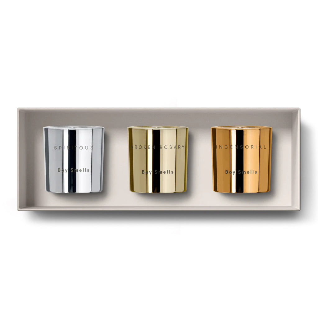 Boy Smells 2023 Limited Edition Holiday scented coconut beeswax votive candle set in metallic silver, gold and rose gold glass vessels with the candle scent and "boy smells" engraved on the front, nestled in a tan gift box with lid off.