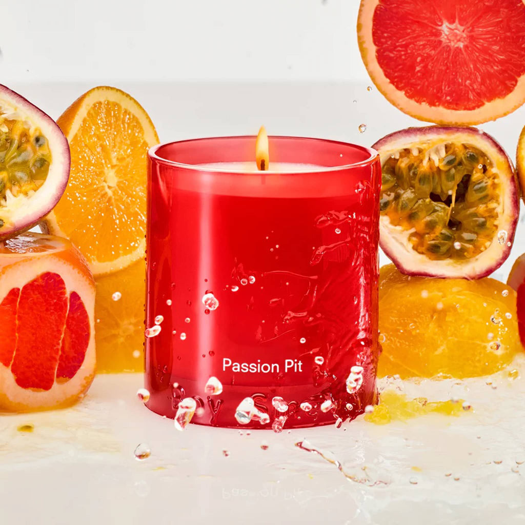 Boy Smells Passion Pit scented 9 ounce Essentials candle in red glass vessel, with citrus and pomegranate fruit slices in background.