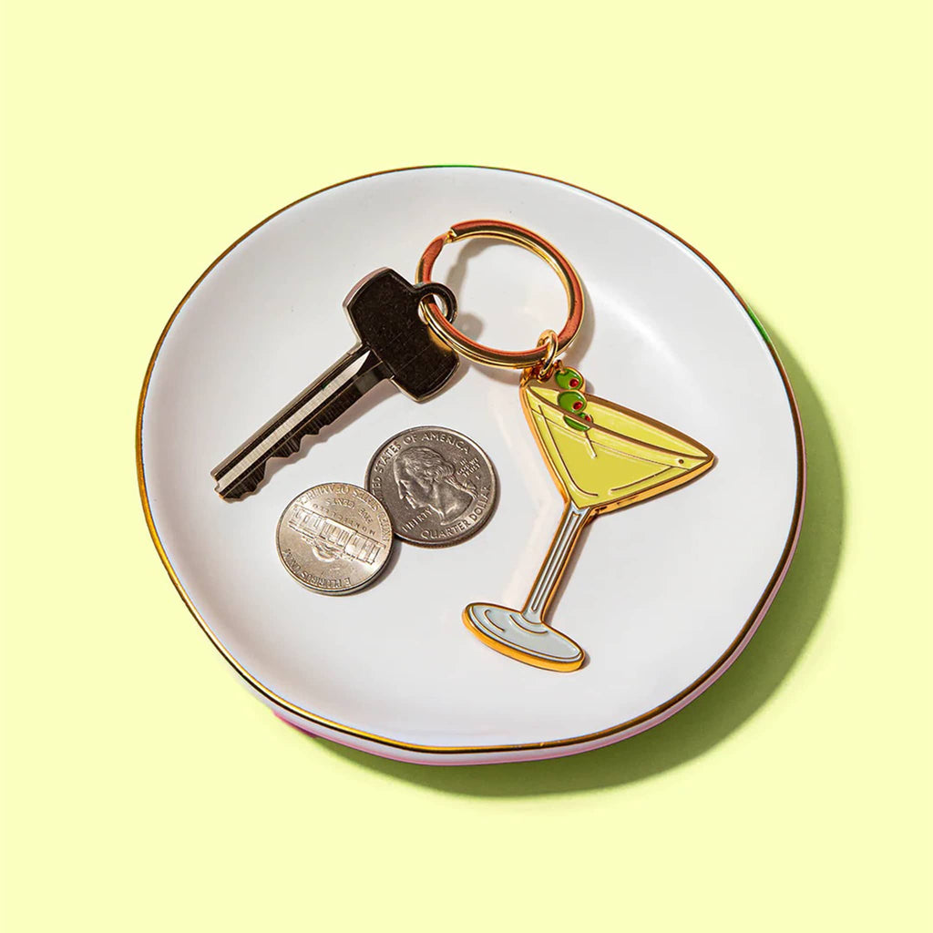 Key, coins, and a martini glass keychain on a white plate with a yellow background.