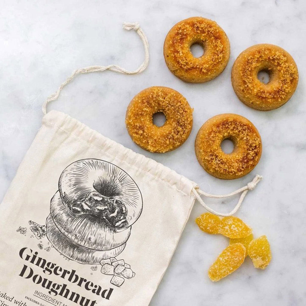 Brooklyn Brewshop Farm Steady Holiday Limited Edition Gingerbread Doughnut Baking Mix in drawstring pouch packaging with baked doughnuts and candied ginger on a marble surface.