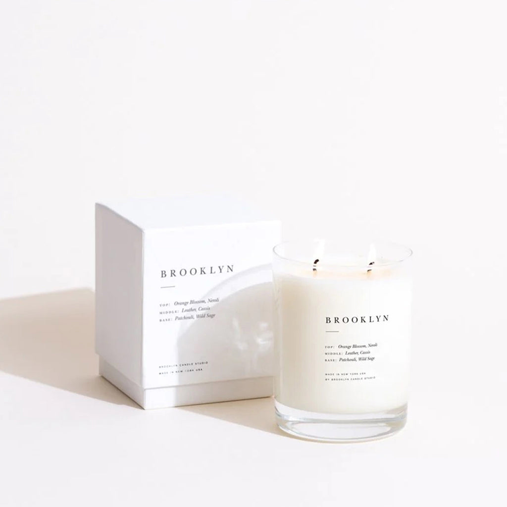 Brooklyn Candle Studio Brooklyn Escapist scented candle in screen printed clear glass vessel with double wicks lit, beside white gift box.