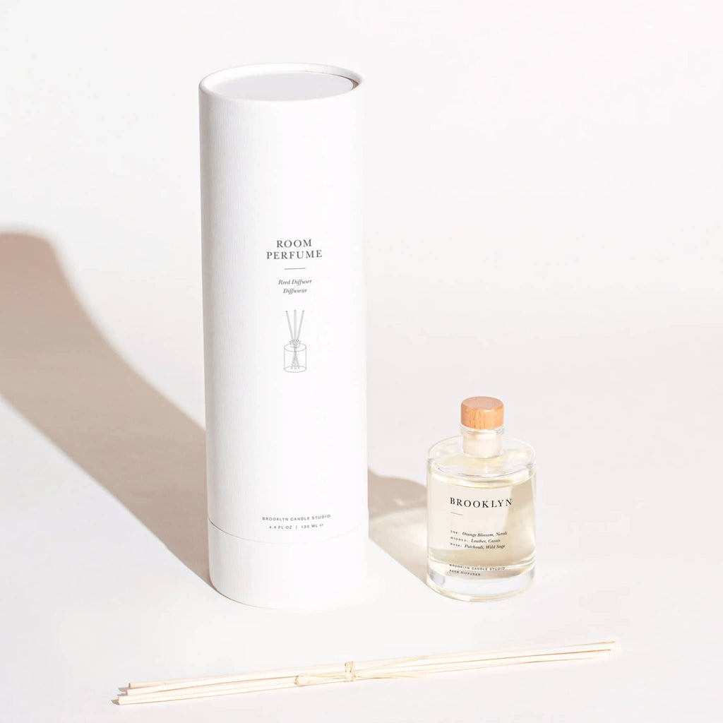 Brooklyn Candle Studio Brooklyn scented reed diffuser room perfume, clear glass bottle with stopper, bundle of reeds and white cylinder packaging.