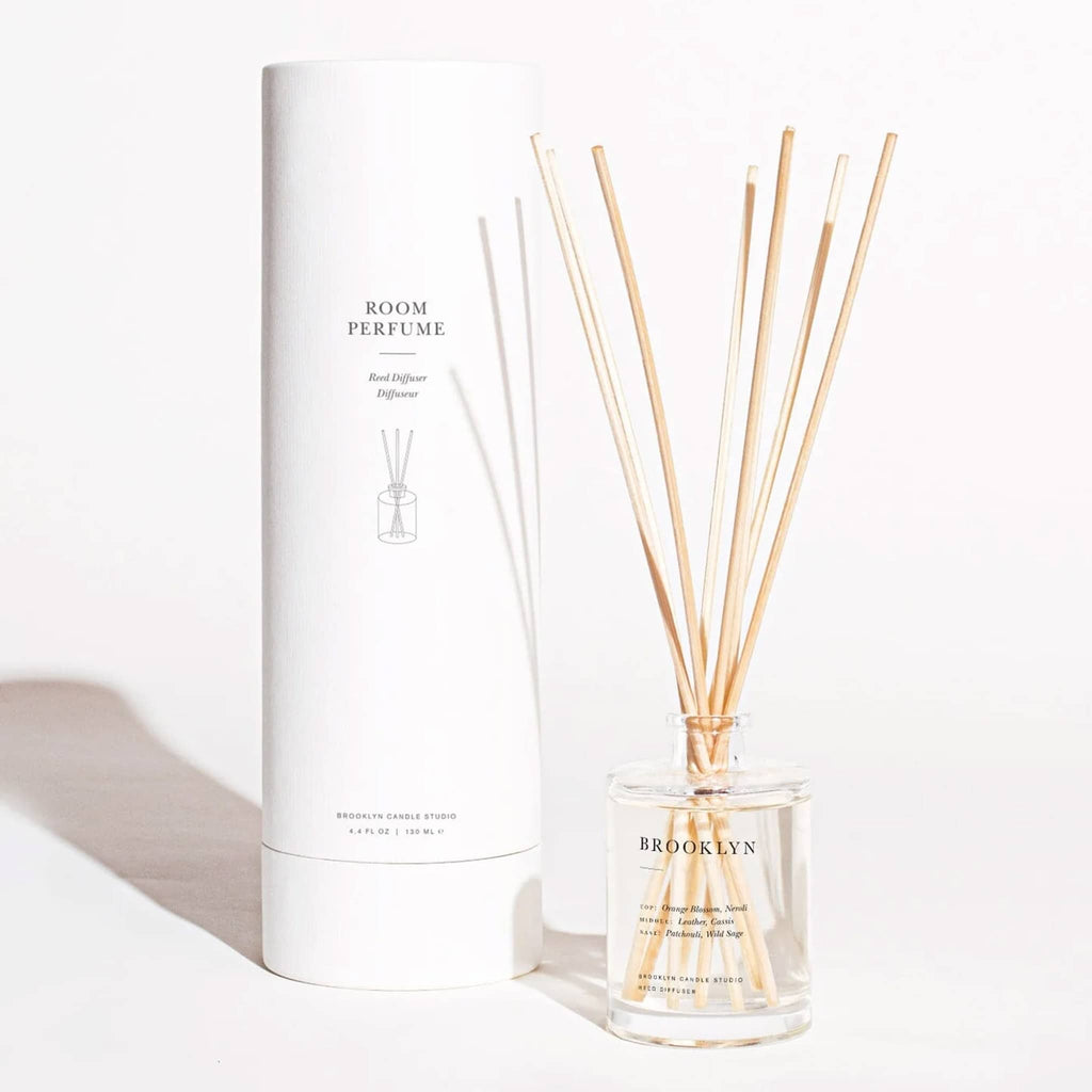 Brooklyn Candle Studio Brooklyn scented reed diffuser room perfume, clear glass bottle with reeds beside white cylinder packaging.