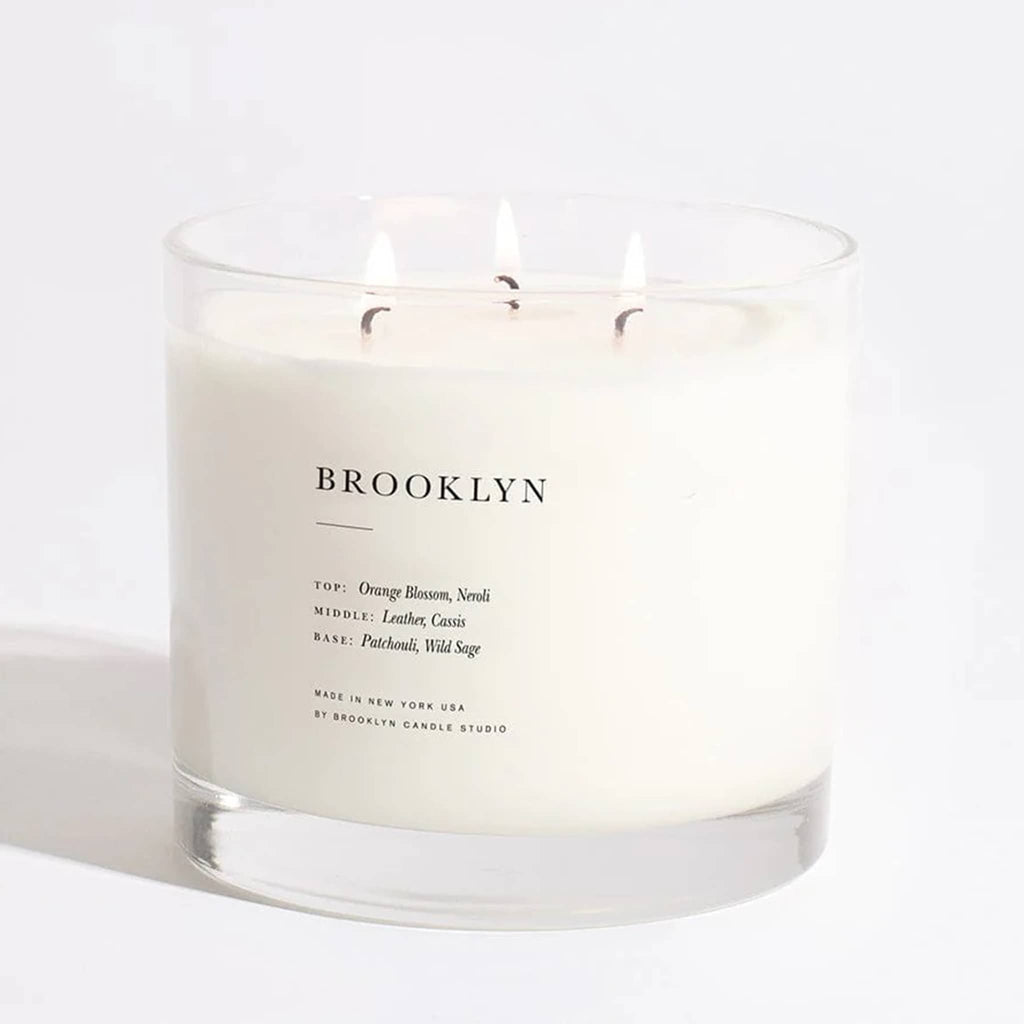 Brooklyn Candle Studio Brooklyn scented triple wick xl maximalist candle in clear glass vessel, wicks are lit.