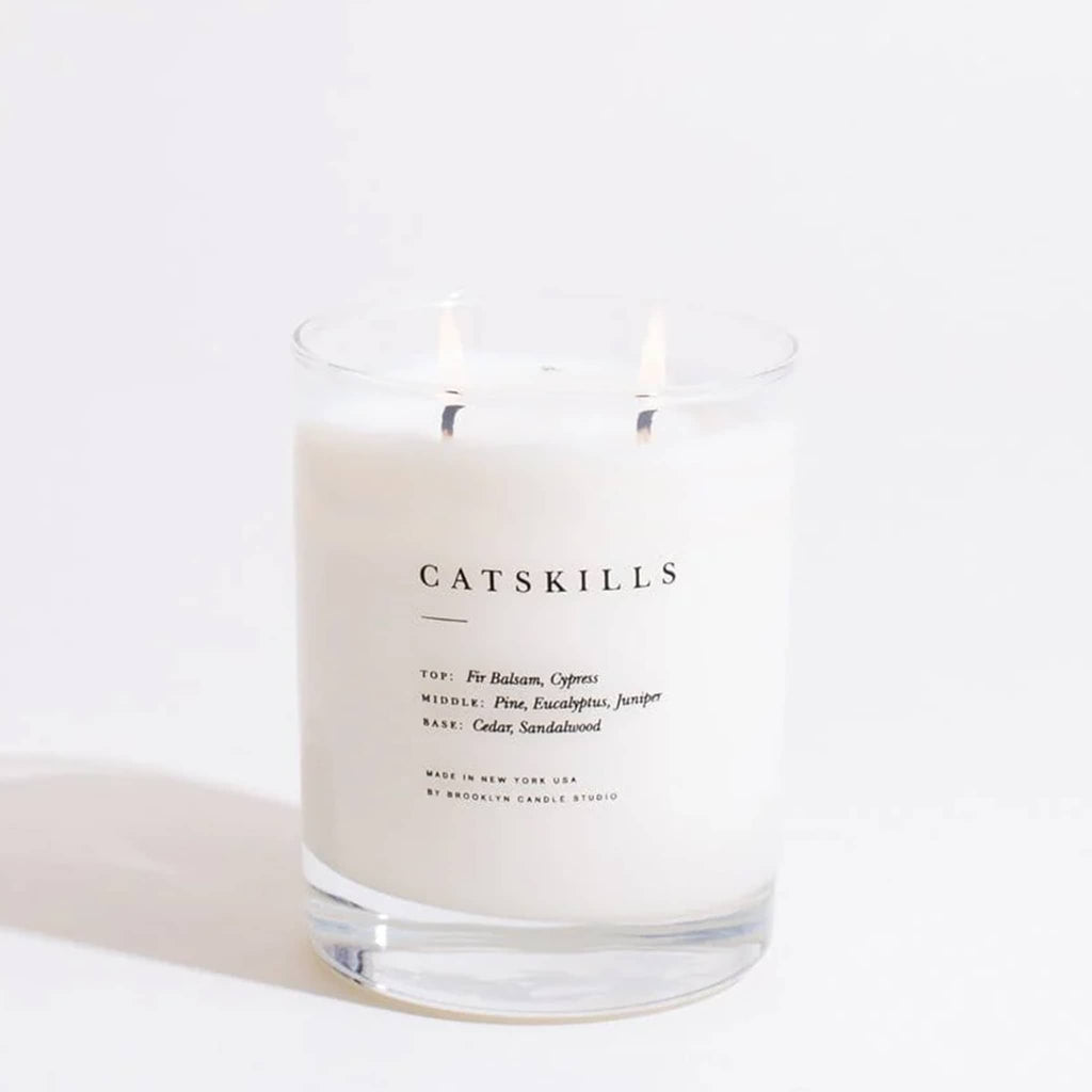 Brooklyn Candle Studio Catskills scented soy wax candle in clear glass vessel with double wicks, wicks are lit.