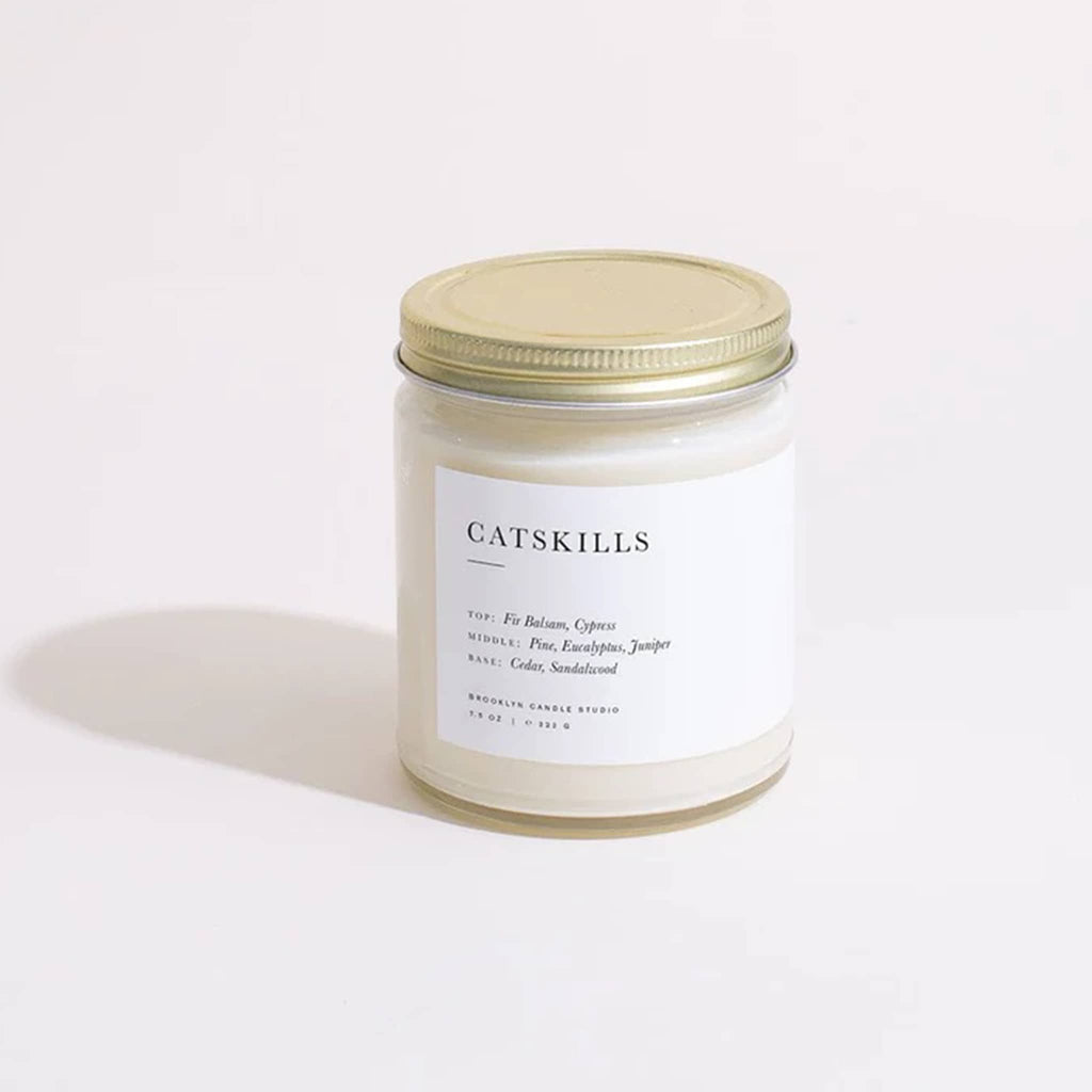 Brooklyn Candle Studio Catskills scented candle in a straight sided clear glass jar with minimalist label and brushed gold screw-on lid.