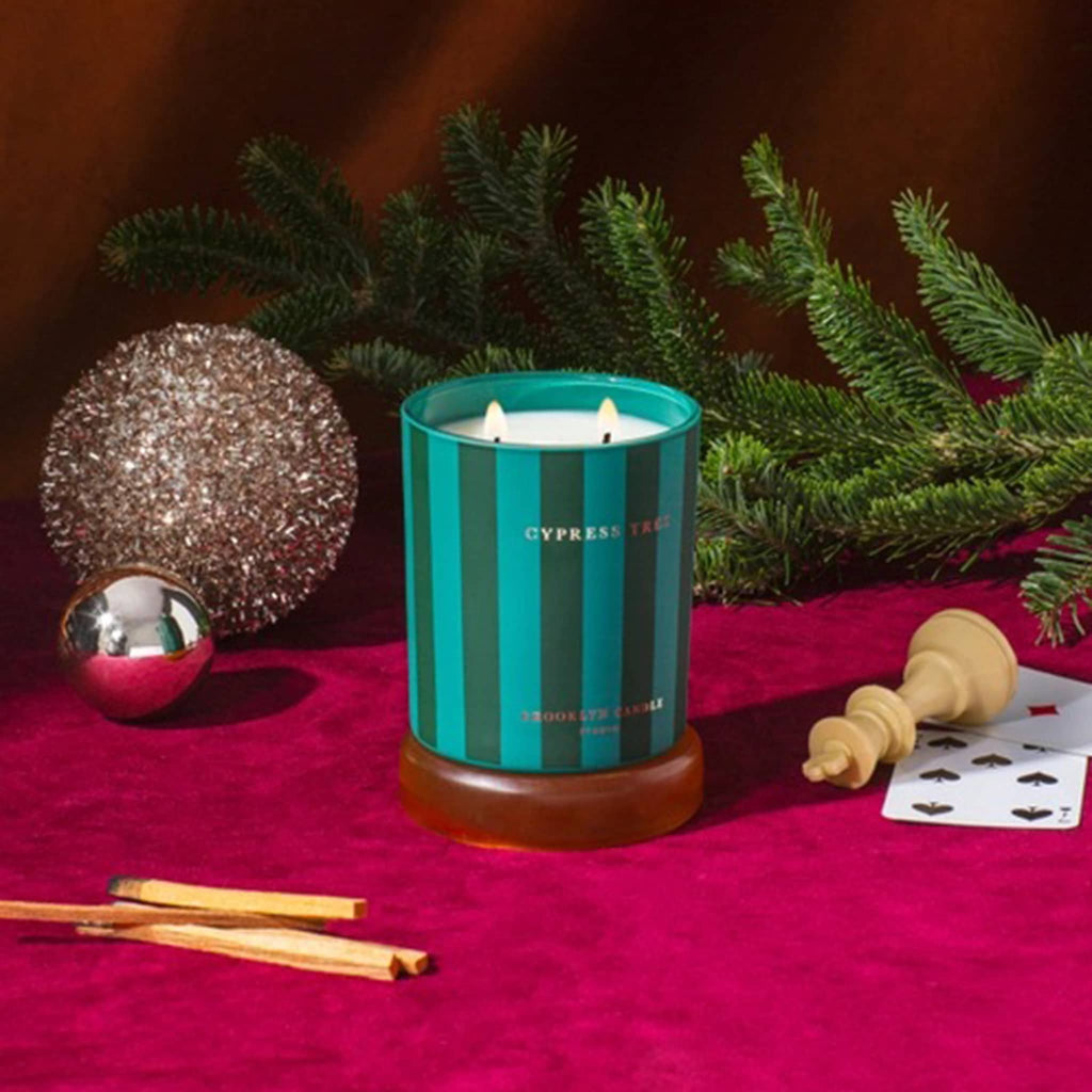 Striped candle with 'Cypress Tree' branding on a red surface with decorative elements.