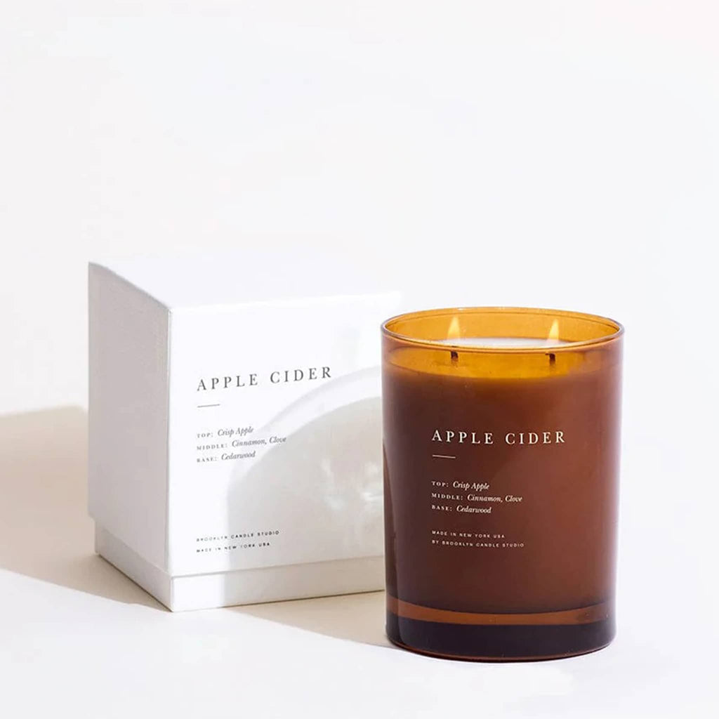 'Apple Cider' scented candle in amber glass vessel with a white box in the background.