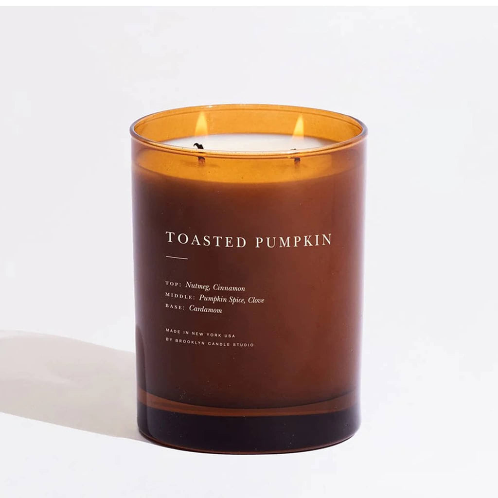 Toasted Pumpkin candle in an amber glass container, two wicks lit, on a white background.