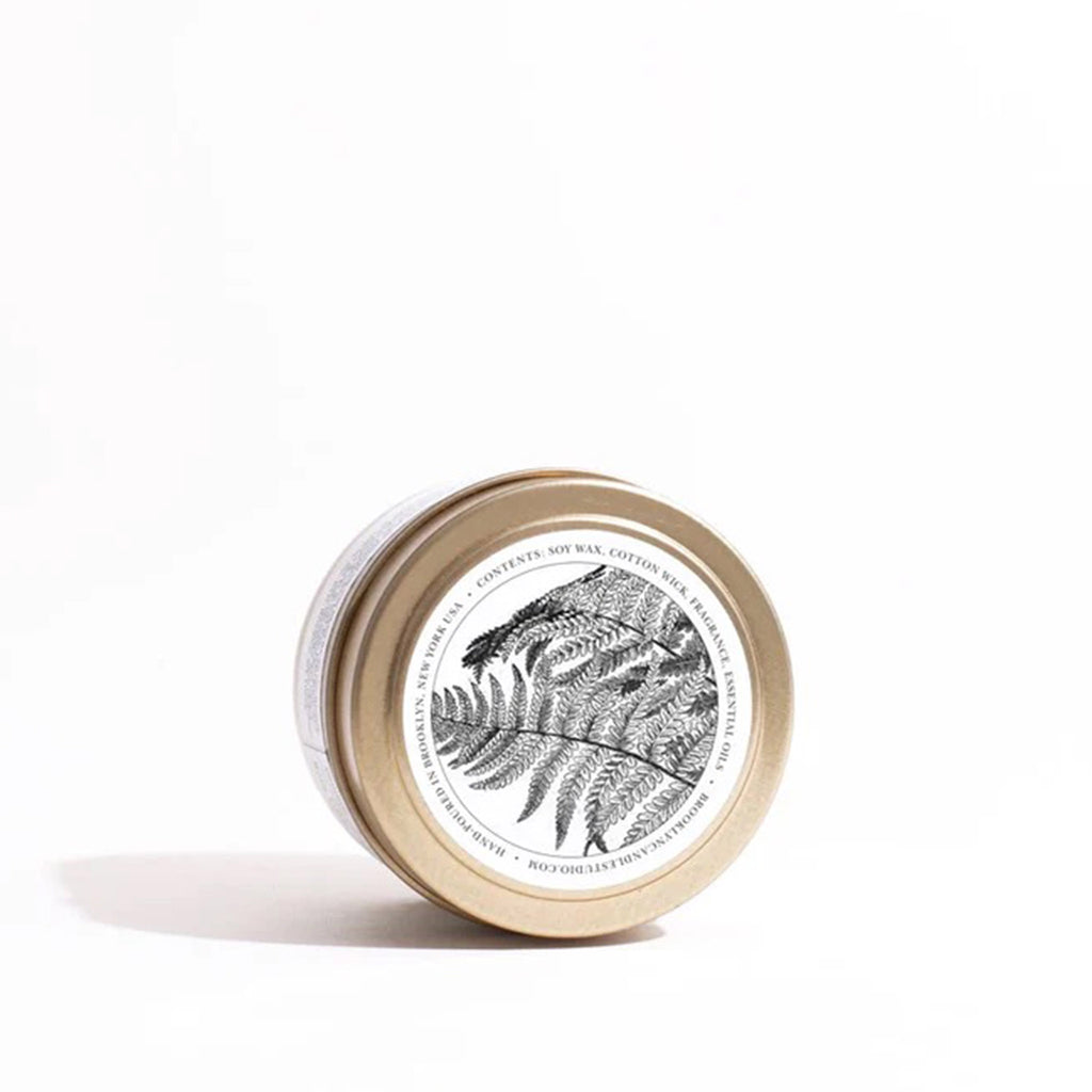 Top of lid of Brooklyn Candle Studio Fern + Moss scented candle in brushed gold travel tin with an illustration of fern leaves.