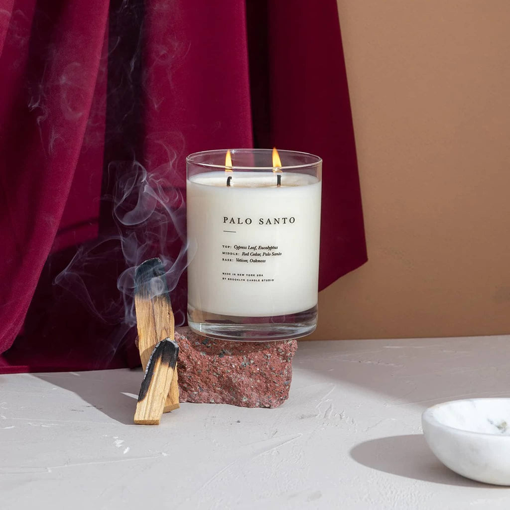Palo Santo candle with burning sticks on a stone holder against a red fabric background.