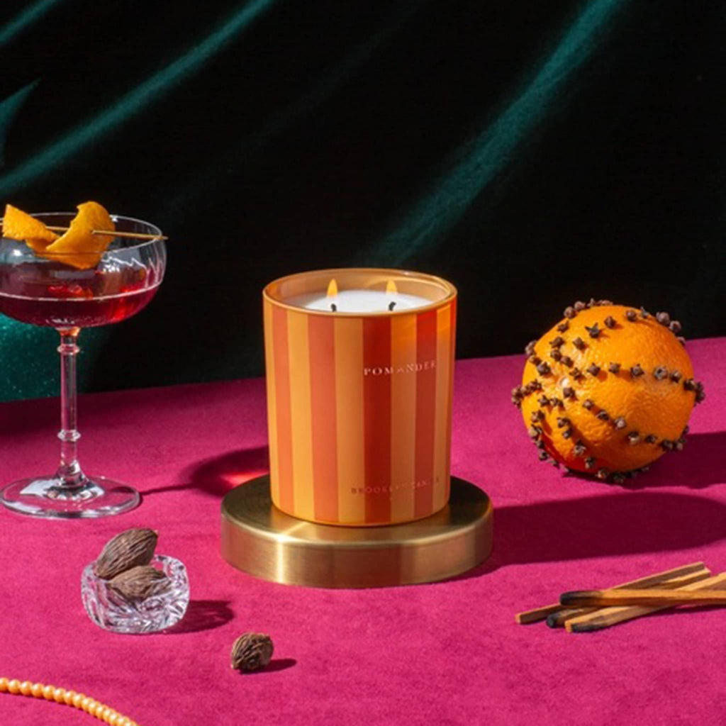 Striped candle on a pink surface with a cocktail and decorative elements.