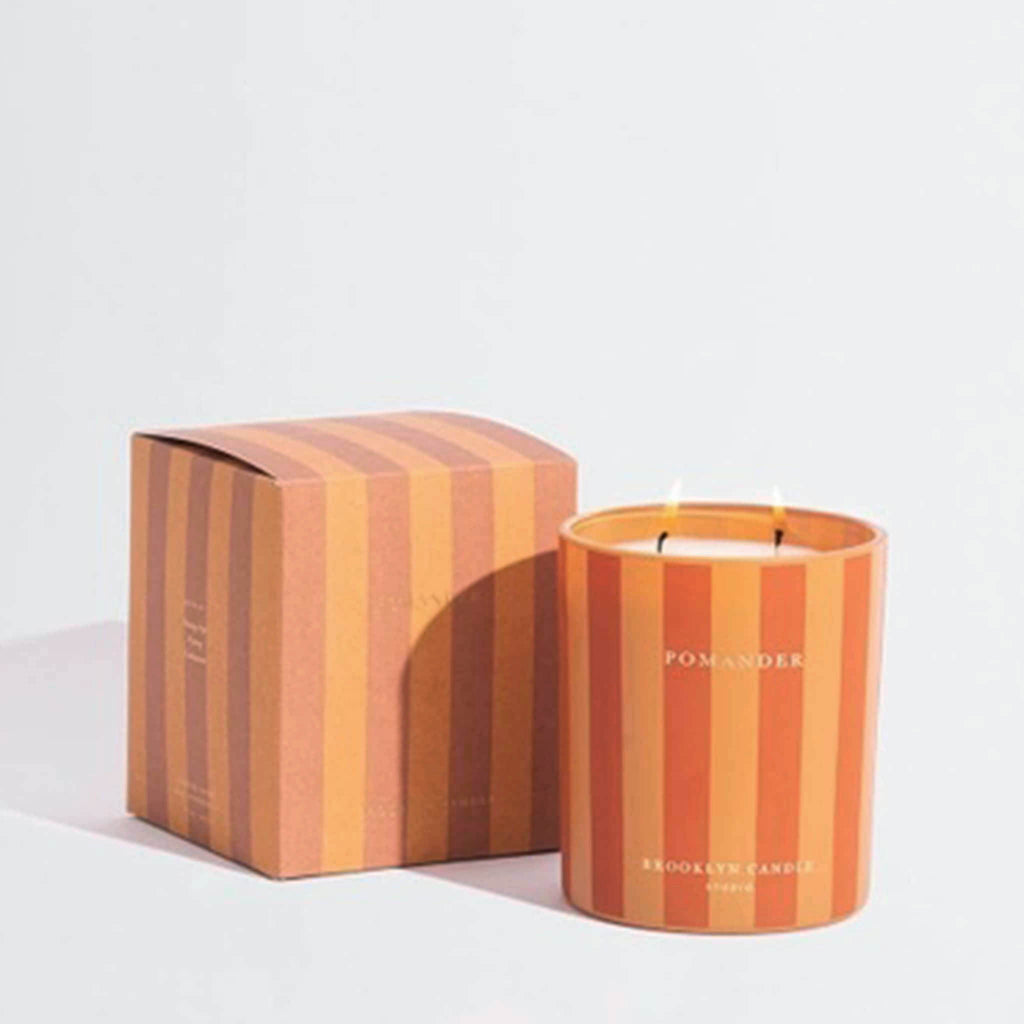 Striped candle and box with 'Pomander' branding on a light gray background.