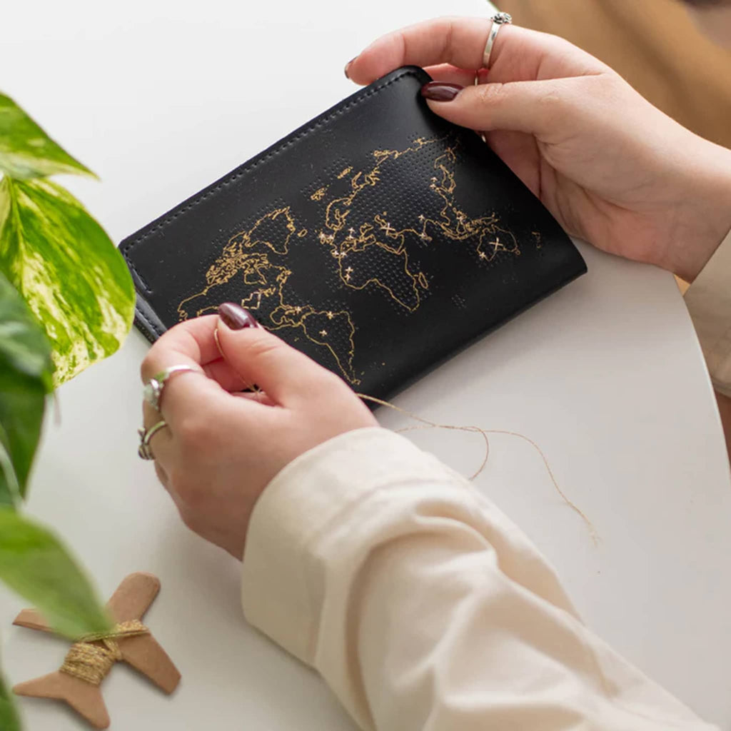 Chasing Threads Black faux leather stitch passport cover with needle and gold thread and person adding stitches.