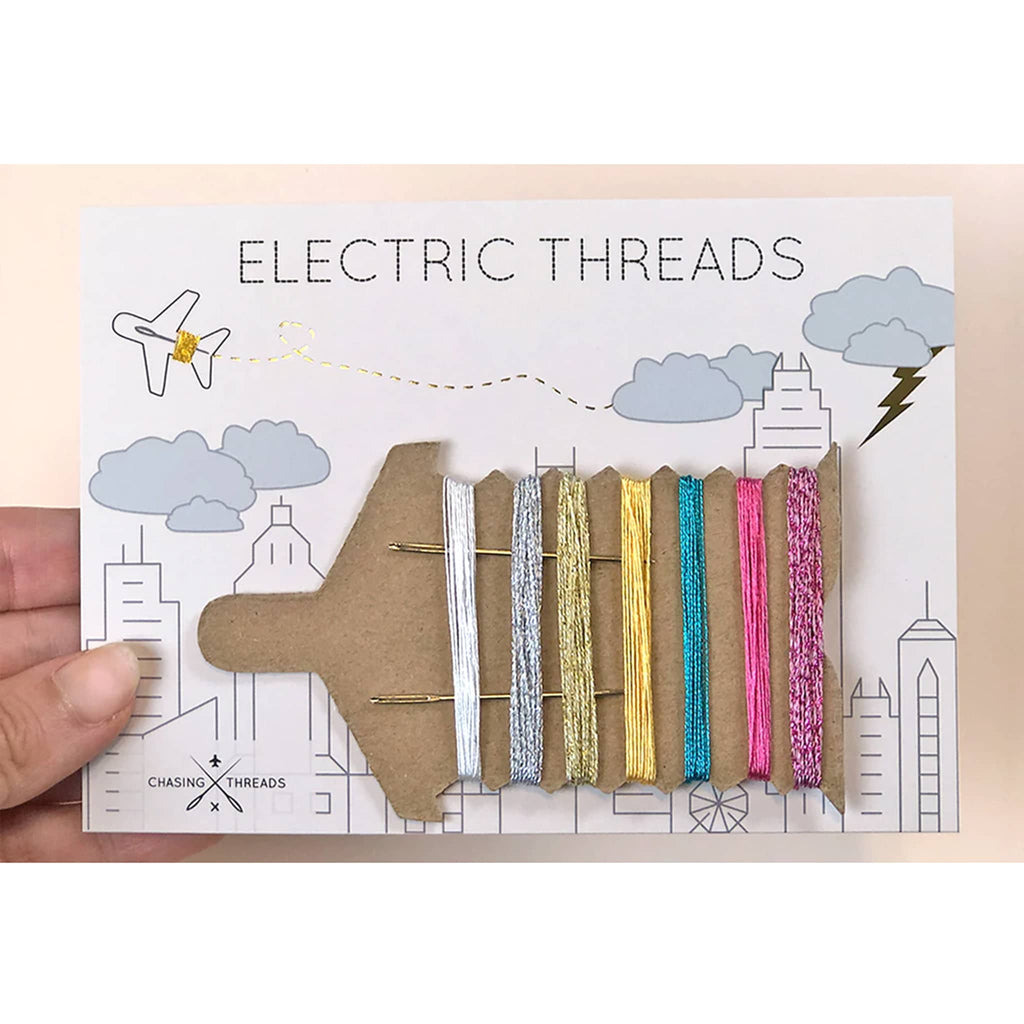 Chasing Threads set of 7 metallic colored threads on plane shaped card on white card packaging with "electric threads" at the top and a skyline illustration.