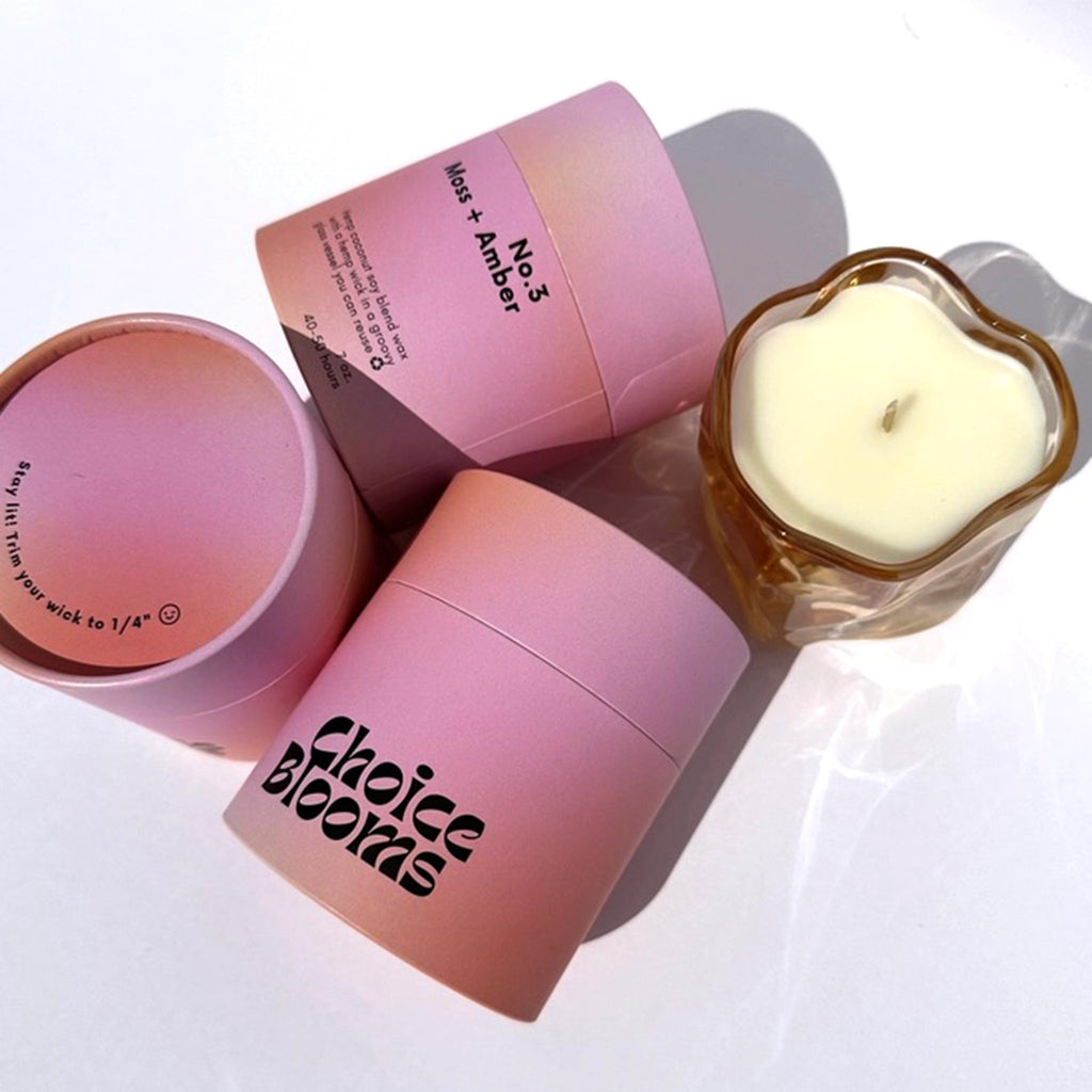 Choice Blooms No. 3 Moss and Amber scented candle made from a hemp, coconut and soy wax blend, in a curvy amber glass vessel surrounded by 3 ombre orange to pink canisters to show all sides of packaging.