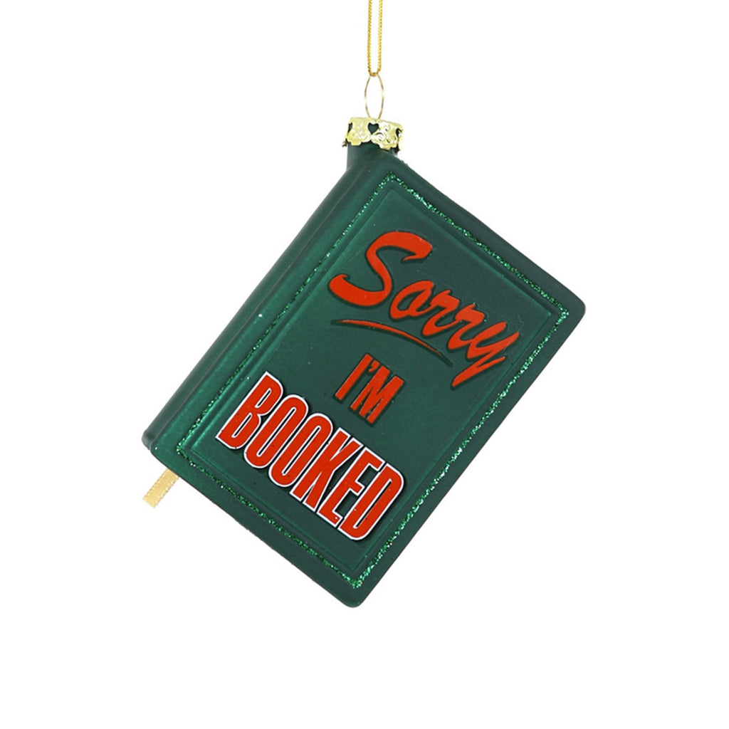 Cody Foster green glass book shaped ornament with "sorry, i'm booked" in red lettering.