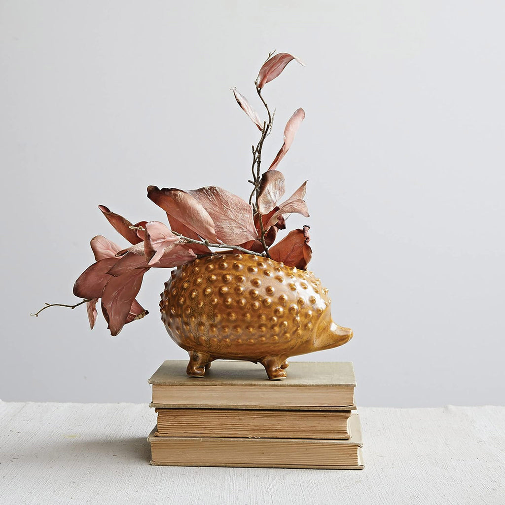 Creative Co-op Brown Stoneware Hedgehog Planter, side view, sitting on a pile of books with dried flowers inside.