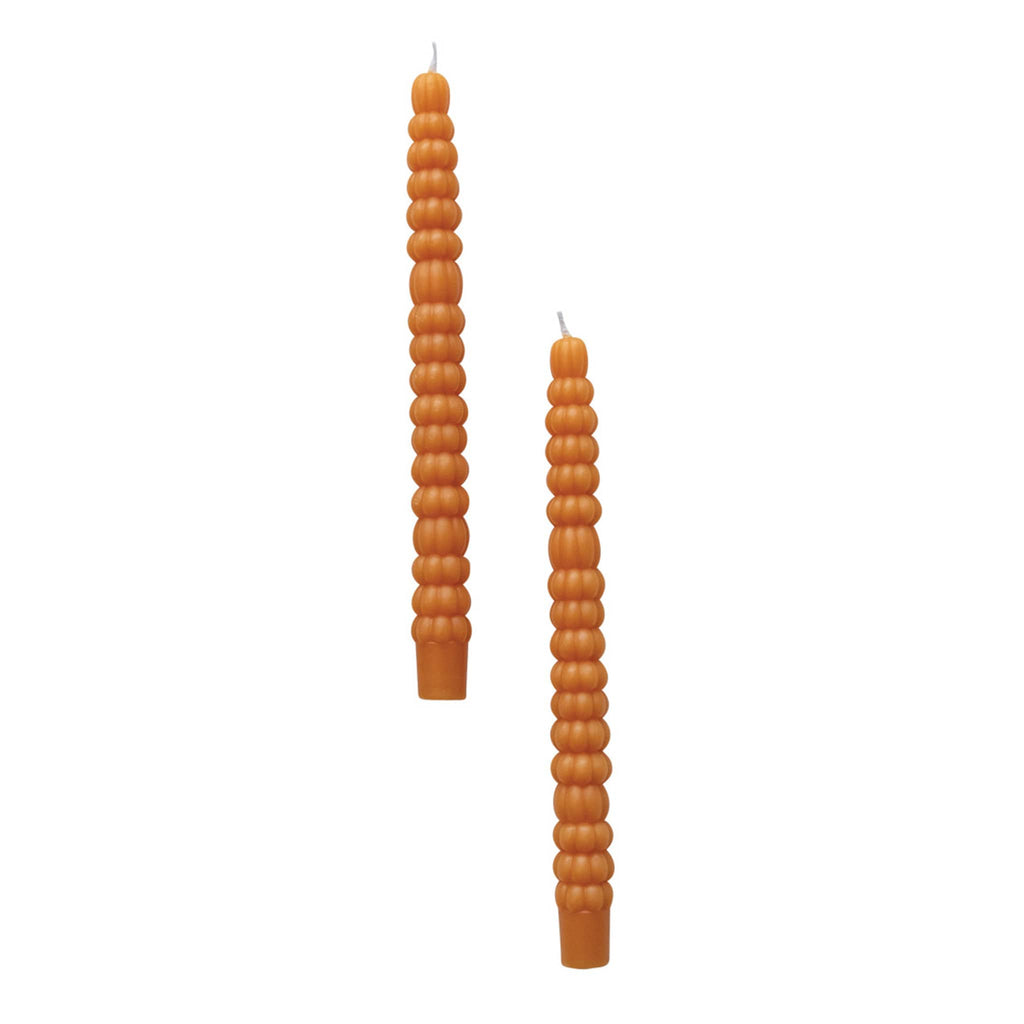 Two orange taper candles that look like stacked pumpkins on a white background.