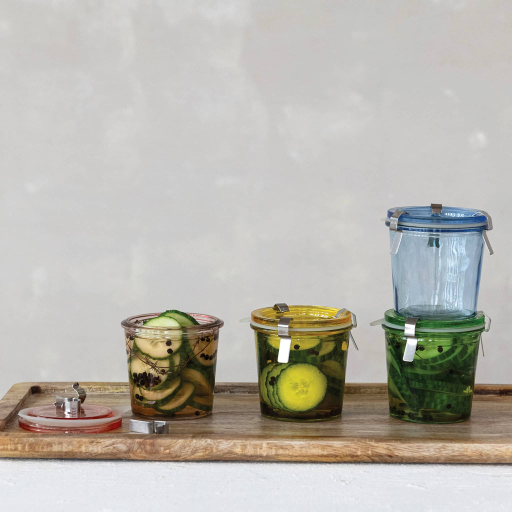 Creative Co-op airtight glass food storage jar in four colors, shown on a wood board with pickles inside.