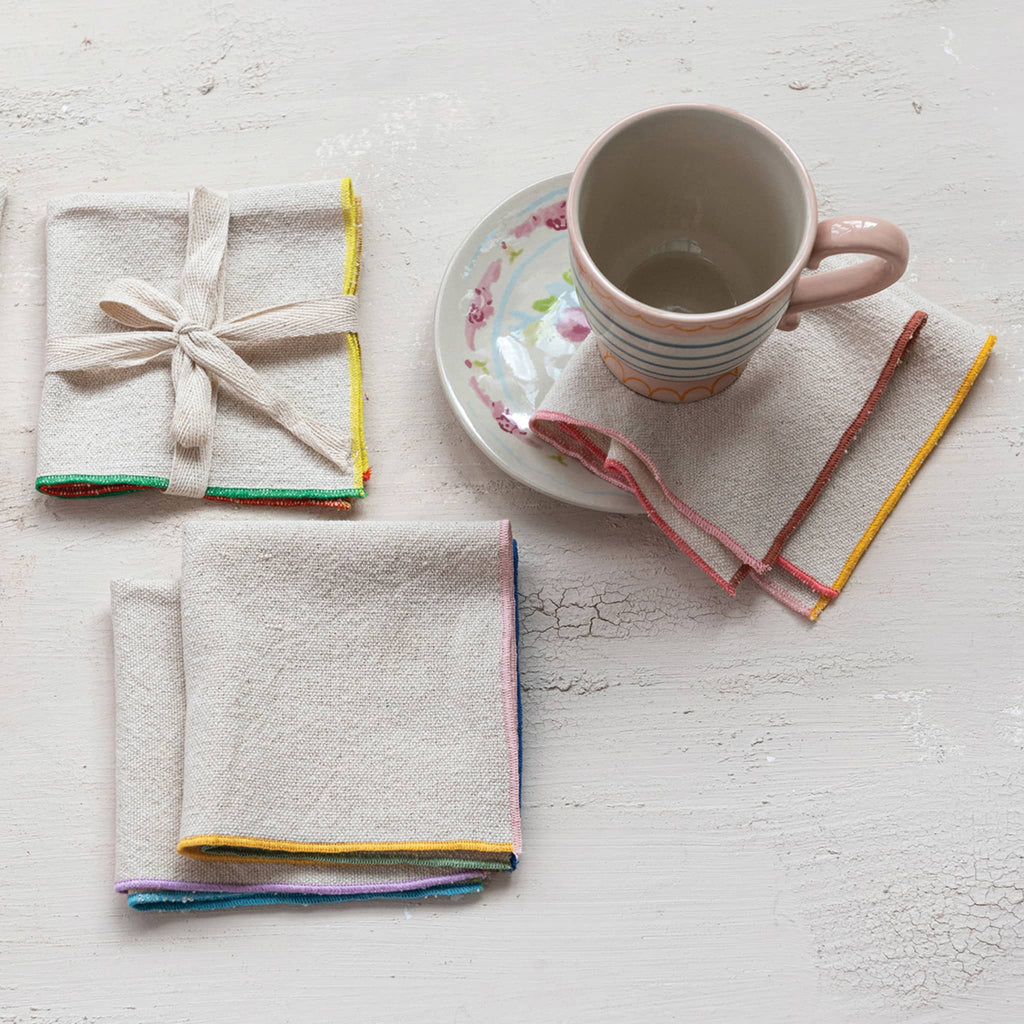 Creative Co-op square woven cotton cocktail napkins with colorful stitched edge, set of four with a mug and saucer.