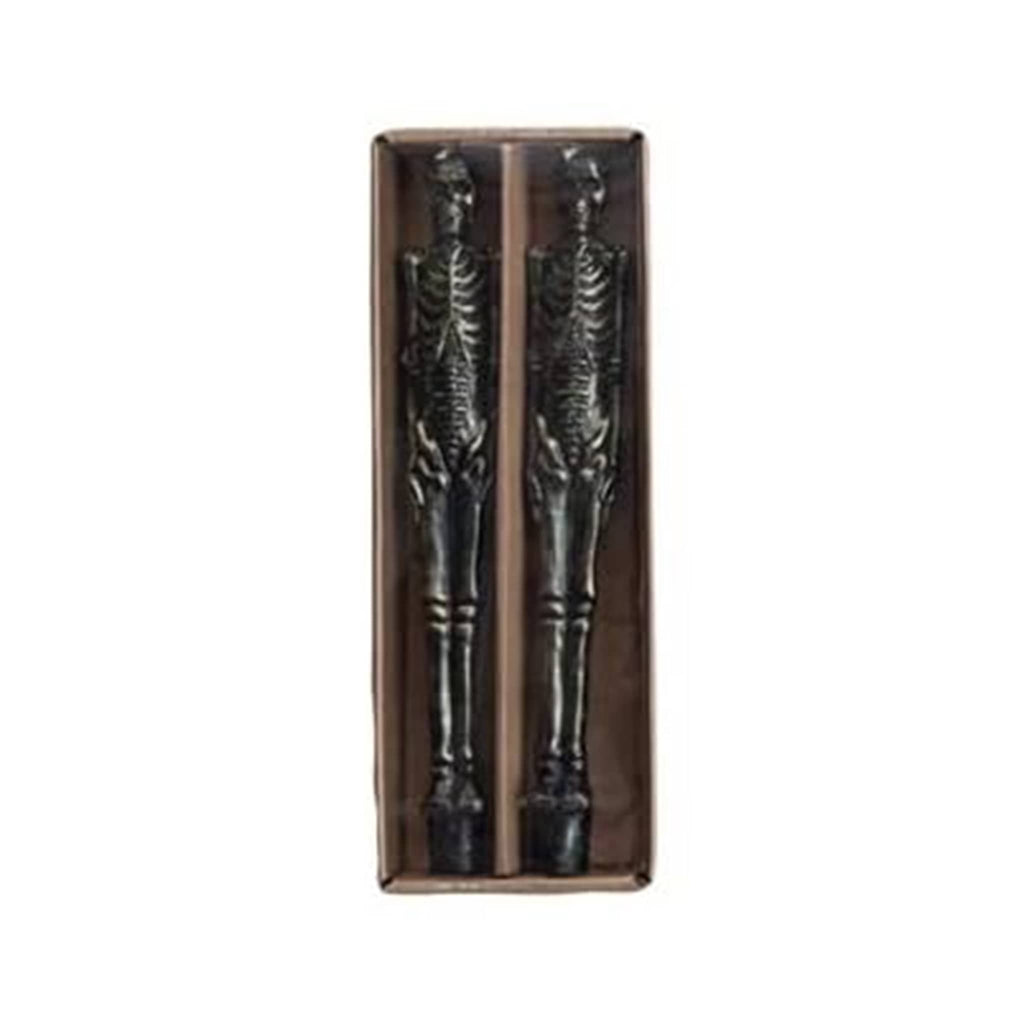 Pair of black skeleton taper candles in a cardboard box on a white background.