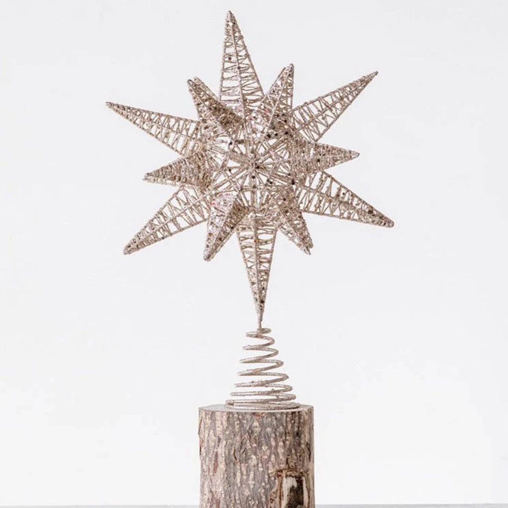 Metal star tree topper with gold glitter finish on a wood log, on a white background.
