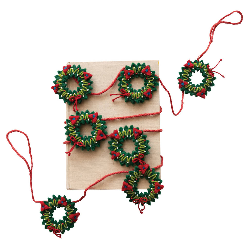 Decorative garland with mini embroidered wreaths and hanging loops at both ends, wrapped around a book, on a white background.