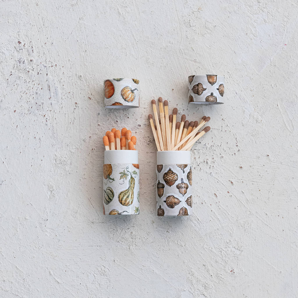 Two sets of matches in fall patterned containers on a light gray surface.